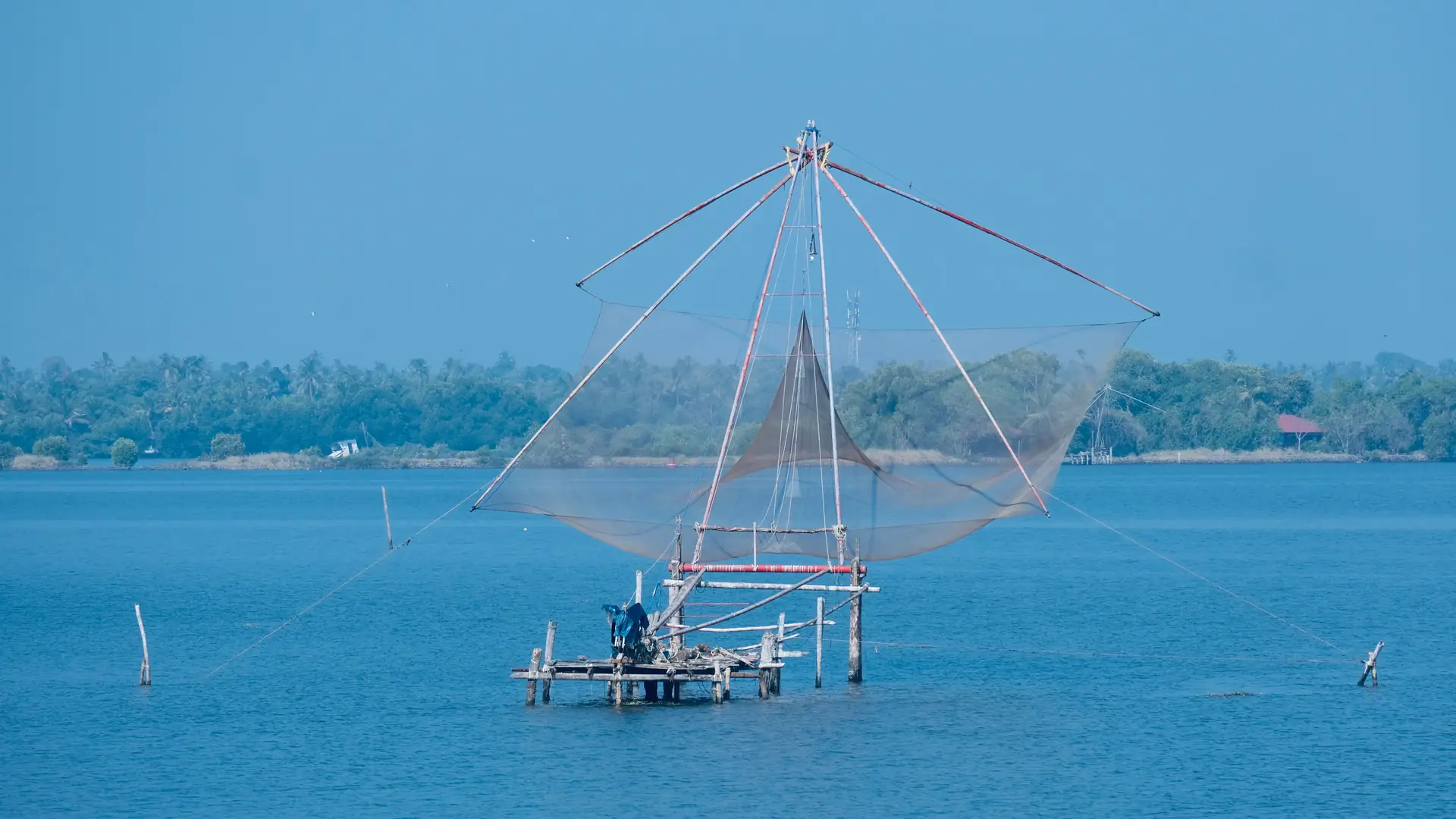 A picturesque view of a large Chinese fishing net on a tranquil coastline under a blue sky