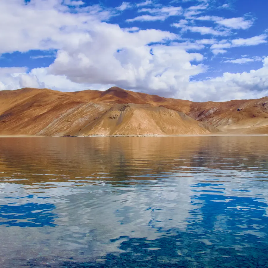 Stunning view of Pangong Tso Lake reflecting arid hills and blue sky. Perfect for travel inspiration