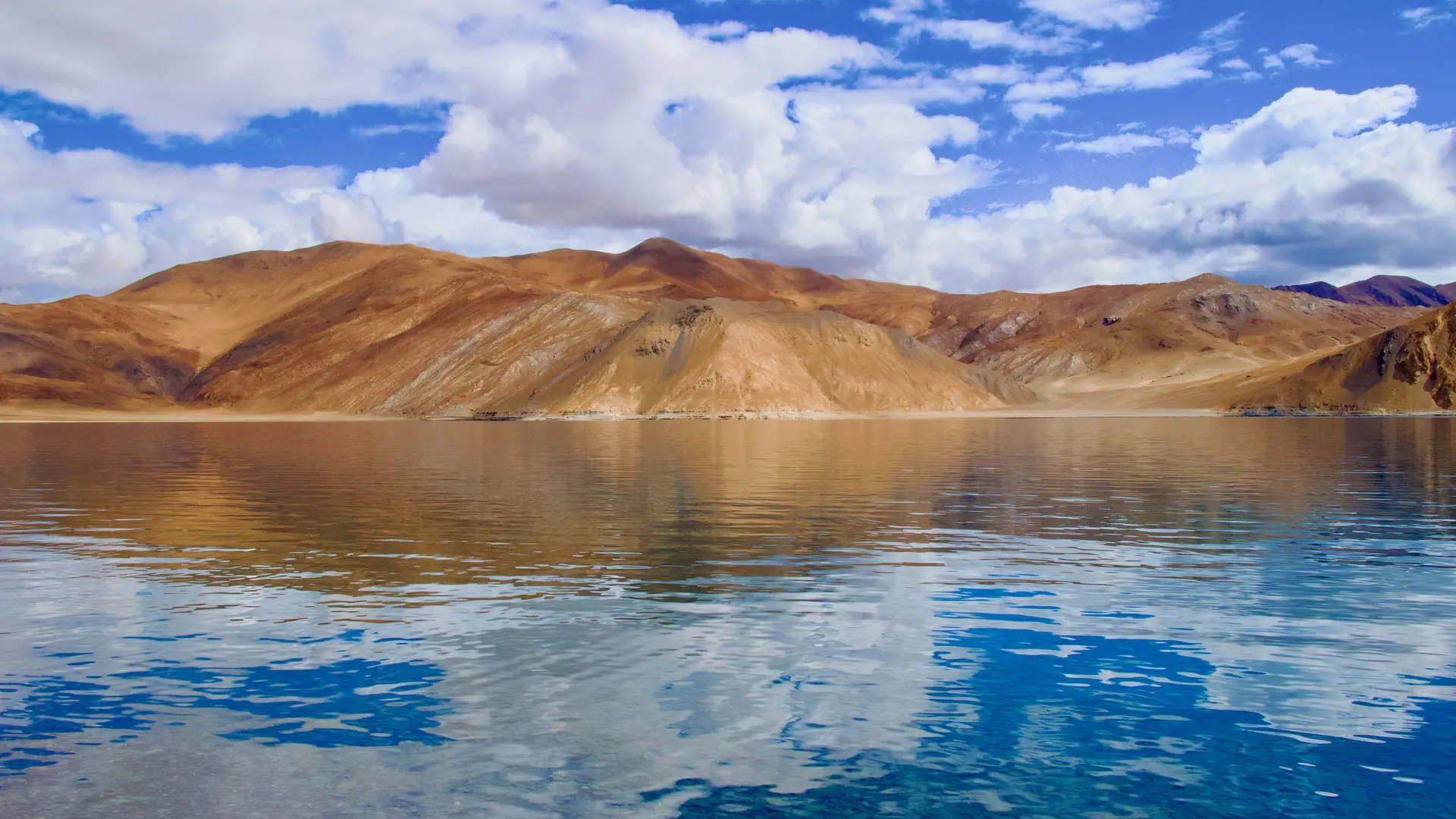 Stunning view of Pangong Tso Lake reflecting arid hills and blue sky. Perfect for travel inspiration