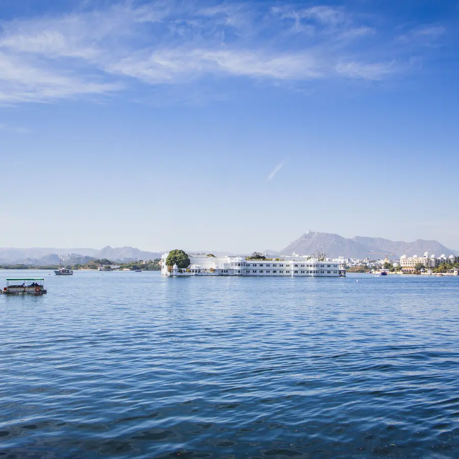 A serene view of Lake Pichola in Udaipur with City Palace in the background under a clear blue sky