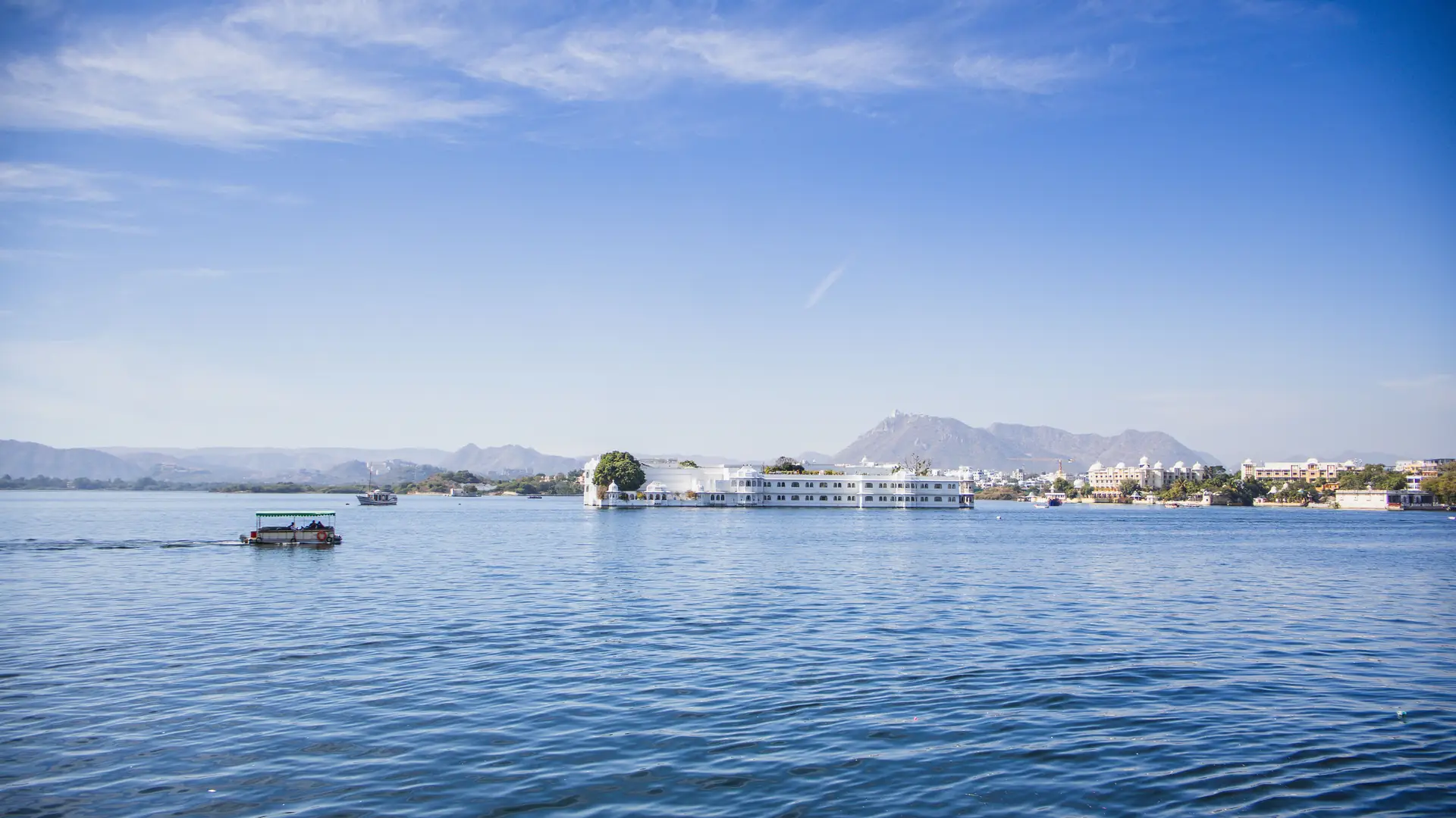 A serene view of Lake Pichola in Udaipur with City Palace in the background under a clear blue sky