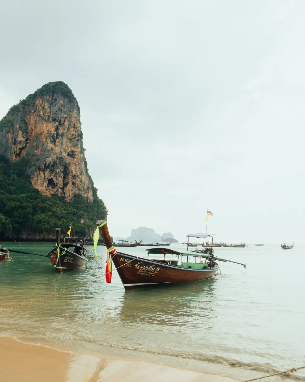 Serene scene of longtail boats moored on Railay Beach with towering cliffs in Thailand